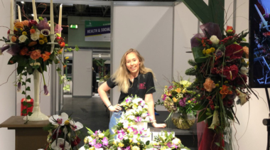 Photo of Clara, Squad UK Floristry competitor standing next to a floral display