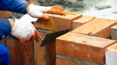 Photo of a bricklayer placing a brick onto a wall