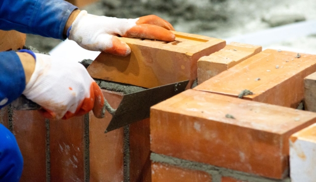 Photo of a bricklayer placing a brick onto a wall