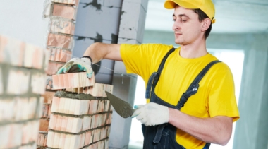 Photo of a young bricklayer placing a brick on to a wall