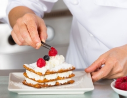 Photo of a confectionery chef placing a raspberry on a mille feuille