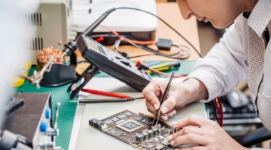 Photo of electronics technician using tweezers on an electronics board