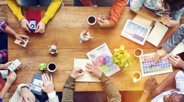 Photo of graphic designers gathered around a table discussing designs