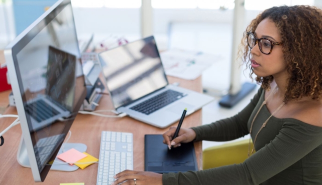 Photo of graphic designer using electronic drawing pad to sketch onto computer