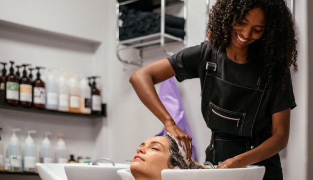 Photo of young hairdresser washing customer's hair in sink