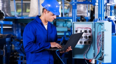 Photo of industrial control technician looking at laptop attached to machinery