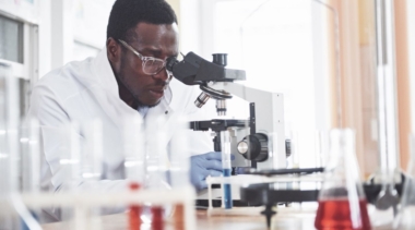 Photo of young lab technician looking into microscope