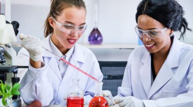 Photo of lab technicians using pipettes to pour liquid into conical flasks