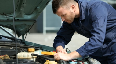 Photo of a young male mechanic examining under the hood of a car