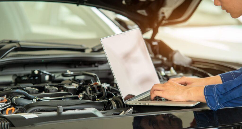 Photo of mechanic using computer to diagnose issues under the hood of the car