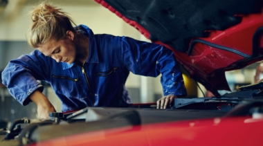 Photo of a young female mechanic examining under the hood of a car