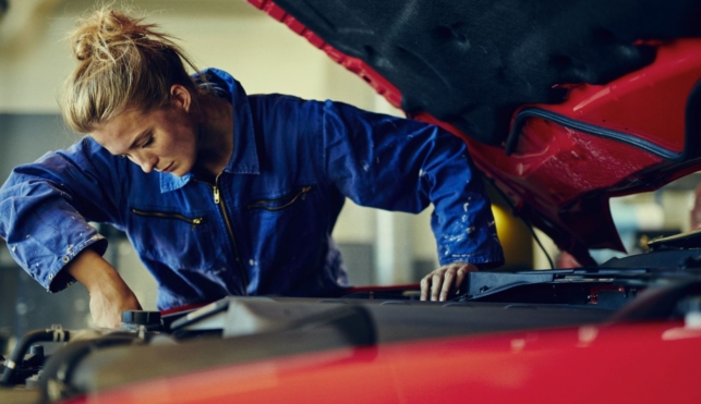 Photo of a young female mechanic examining under the hood of a car