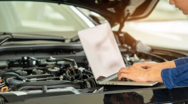 Photo of mechanic using computer to diagnose issues under the hood of the car