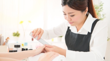 Photo of a young nail technician filing a customer's fingernails in a salon