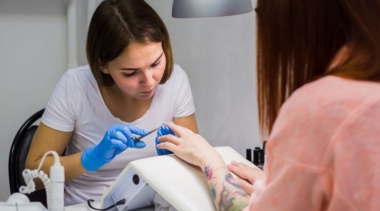 Photo of a young nail technician wearing gloves and cutting a customer's nails