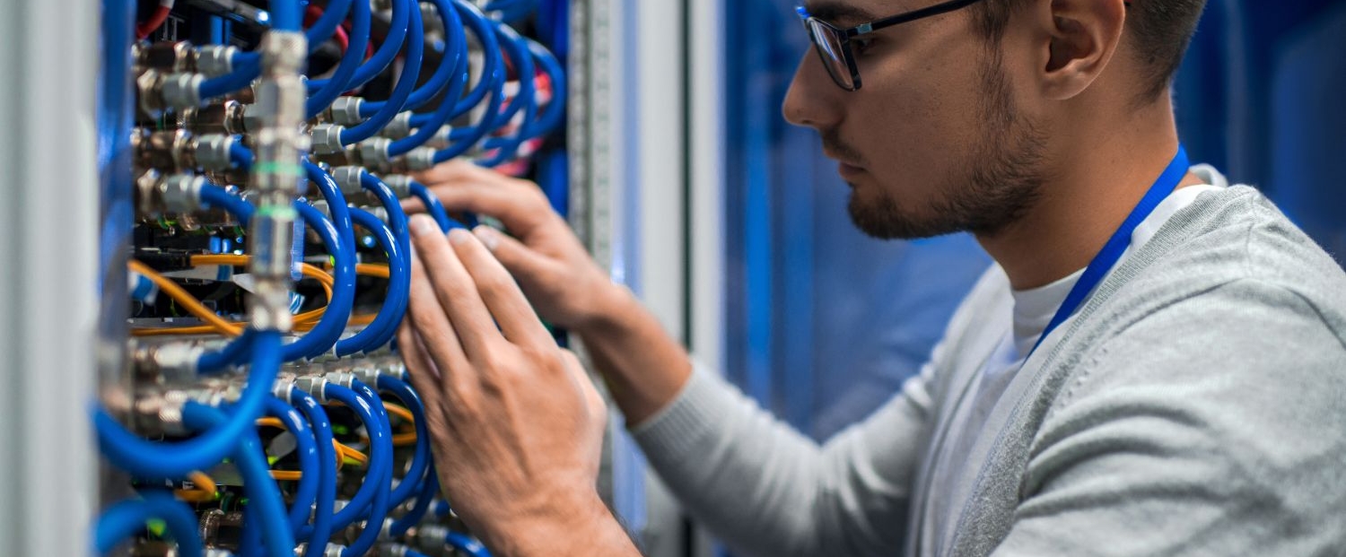 Photo of a young network systems administrator examining a panel of wires