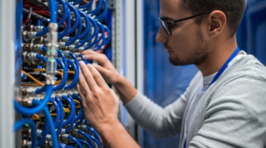 Photo of a young network systems administrator examining a panel of wires