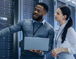 Photo of two network systems administrators examining a data centre and holding a computer