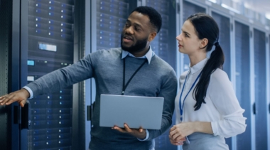 Photo of two network systems administrators examining a data centre and holding a computer