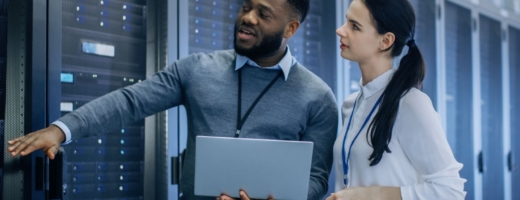 Photo of two network systems administrators examining a data centre and holding a computer