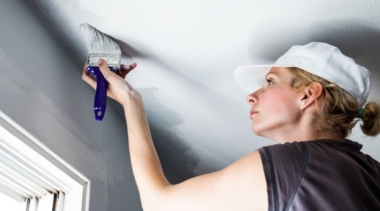 Photo of a young painter and decorator painting a ceiling with a brush