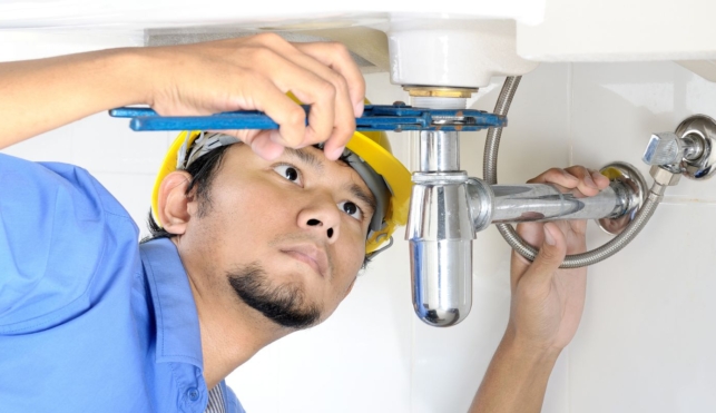 Photo of a young plumber examining the underside of a sink with some tools