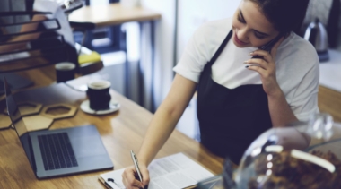 Photo of a young restaurant manager in an apron taking bookings over the phone