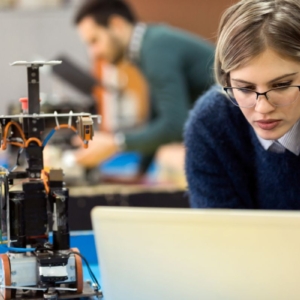 Photo of a young robotics engineer next to a robot and typing into a computer