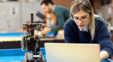 Photo of a young robotics engineer next to a robot and typing into a computer