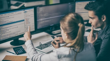 Photo of two young software developers looking at code on a computer screen