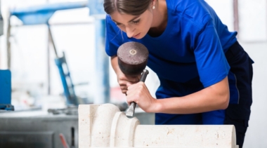Photo of a young female stonemason with a chisel on part of a pillar