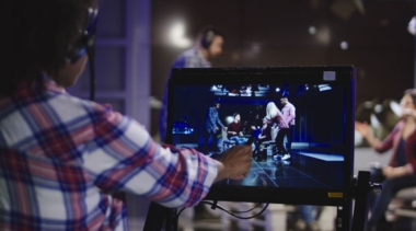 Photo of a young TV producer standing behind a screen filming a scene