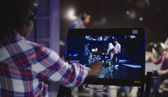 Photo of a young TV producer standing behind a screen filming a scene