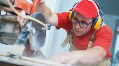 Photo of a young tiler cutting a tile with ear defenders on