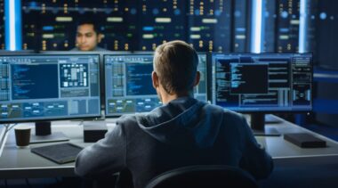 Photo of network systems administrator looking at 3 computer screens