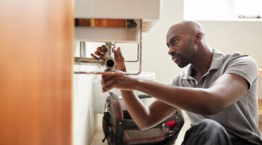 Photo of plumber examining under the sink pipework