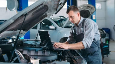 Photo of car mechanic using a computer laptop to diagnosing and checking up on car engines parts for fixing and repair